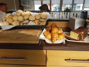 Una mesa de buffet con una variedad de productos de panadería, incluyendo bollos, croissants y un pastel de chocolate.