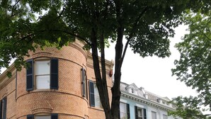 Un edificio ad angolo con facciata in mattoni, un albero di fronte e un edificio blu dall'altra parte della strada.