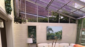 Un'accogliente area patio con un tavolo rotondo ricoperto da una tovaglia floreale, circondata da sedie in vimini e un divano imbottito.