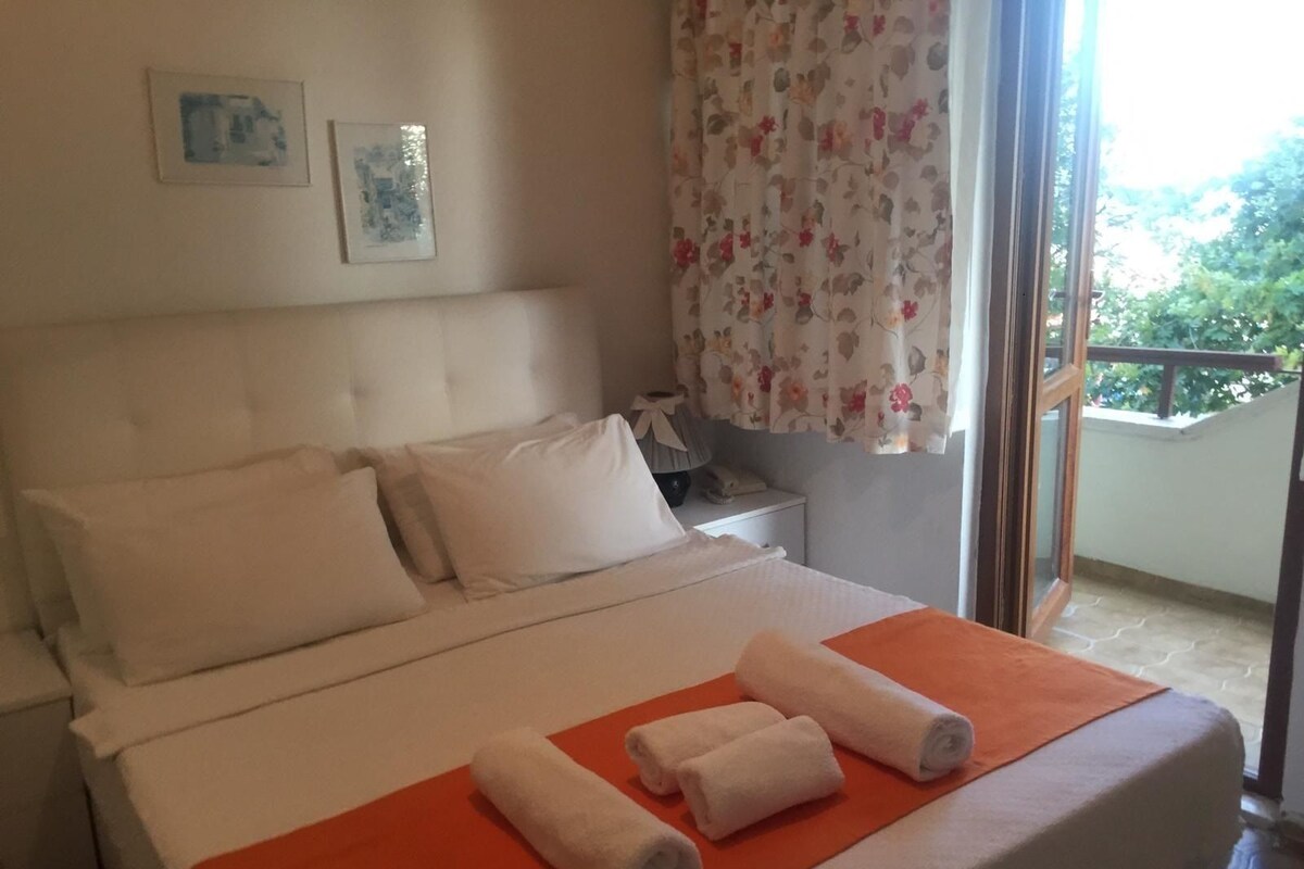Ein Hotelzimmer mit Bett, Kissen, einem Nachttisch, einem Telefon und einem Fenster mit floralem Vorhang.