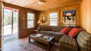 Ein gemütliches Blockhaus-Interieur mit Holzbalkendecke, einer Couch, einem Couchtisch und einem Fenster mit Vorhang.