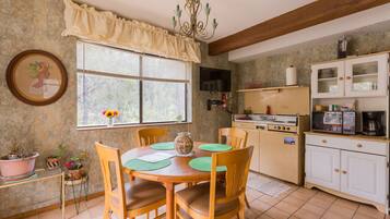 A kitchen with wooden chairs, a dining table, a chandelier, a window with blinds, and a microwave.