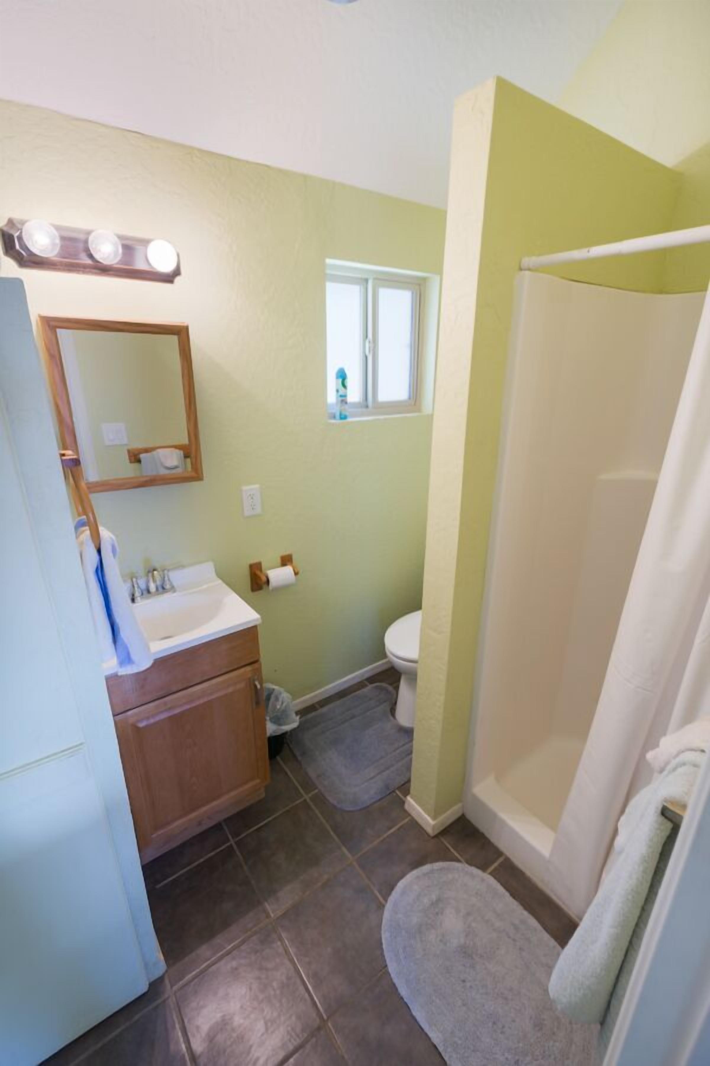 A bathroom with a sink, mirror, vanity, toilet, shower, and a window.