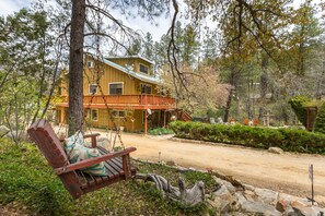 Un chalet rustique doté d’une véranda, entouré d’arbres et agrémenté d’une balançoire.