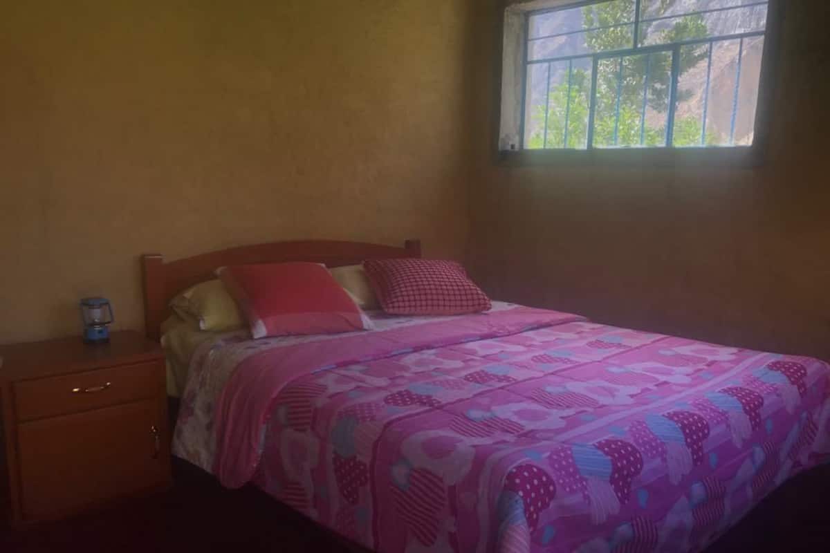 Un dormitorio con cama, mesita de noche, ventana y puerta.