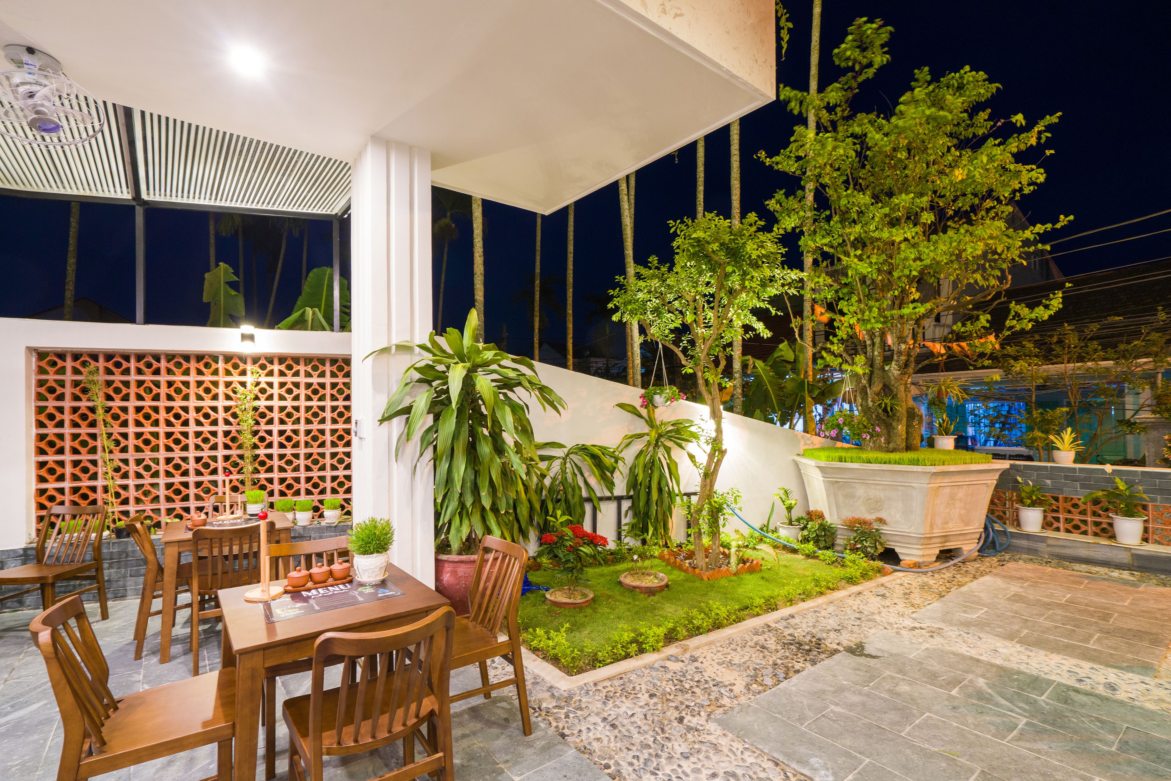 An outdoor dining area with wooden tables and chairs, surrounded by potted plants and a small garden.