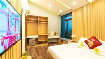 A modern hotel room with a bed, bedside table, TV, wardrobe, and a small desk area.