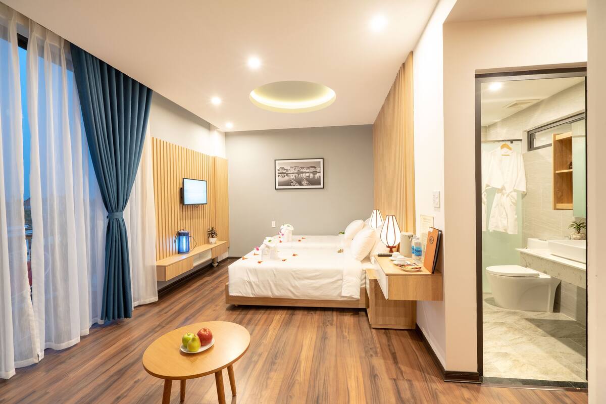 A hotel room with a bed, bedside table, TV, and a small table with fruit.
