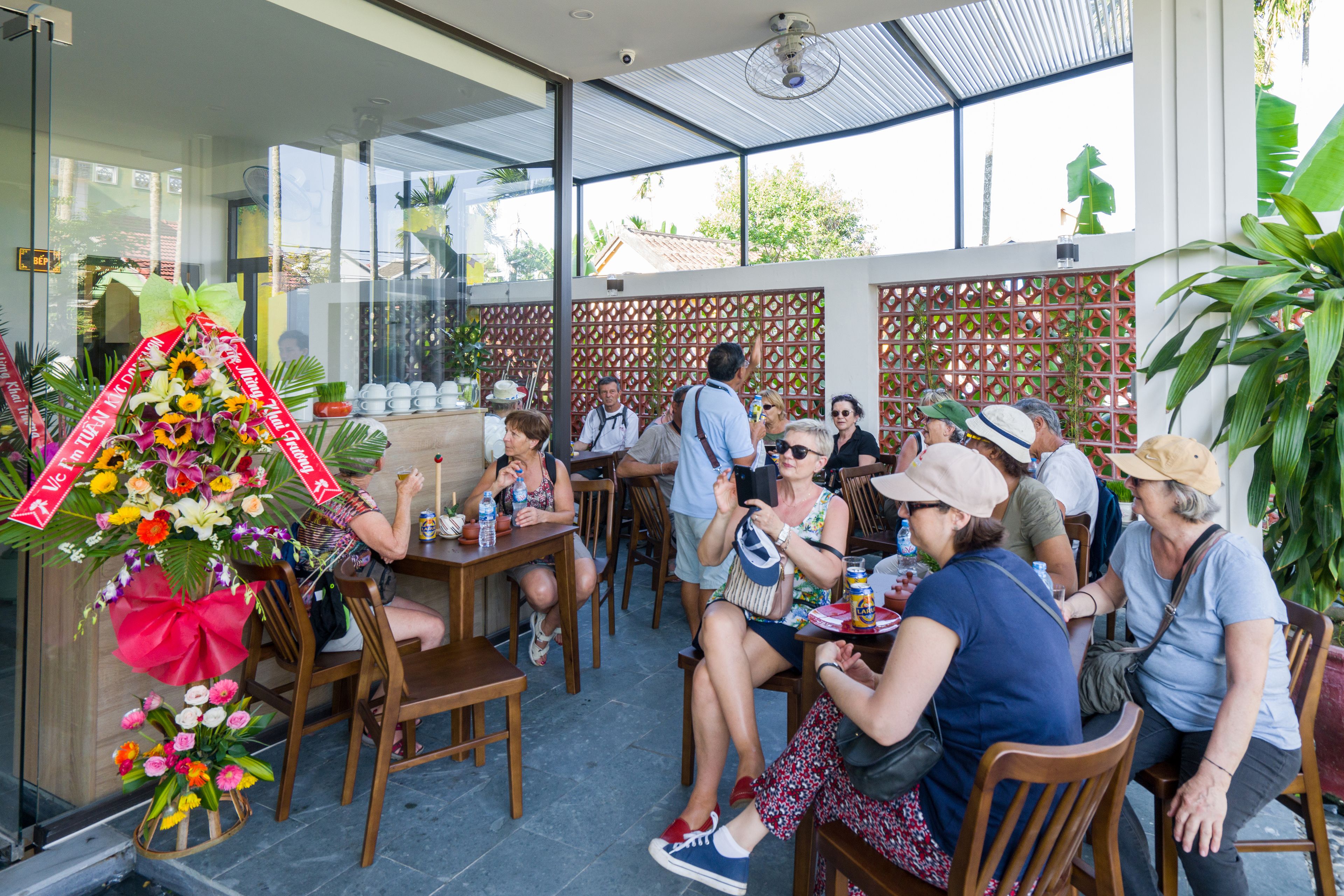 An outdoor dining area with wooden tables and chairs, surrounded by a glass enclosure with a view of the outside.
