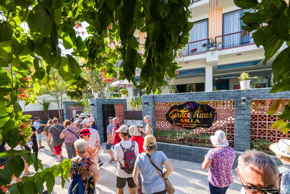 A group of people walking past a building with a sign that reads "Grace River Villas." - Hoi An Grace River Villa (Da Nang)