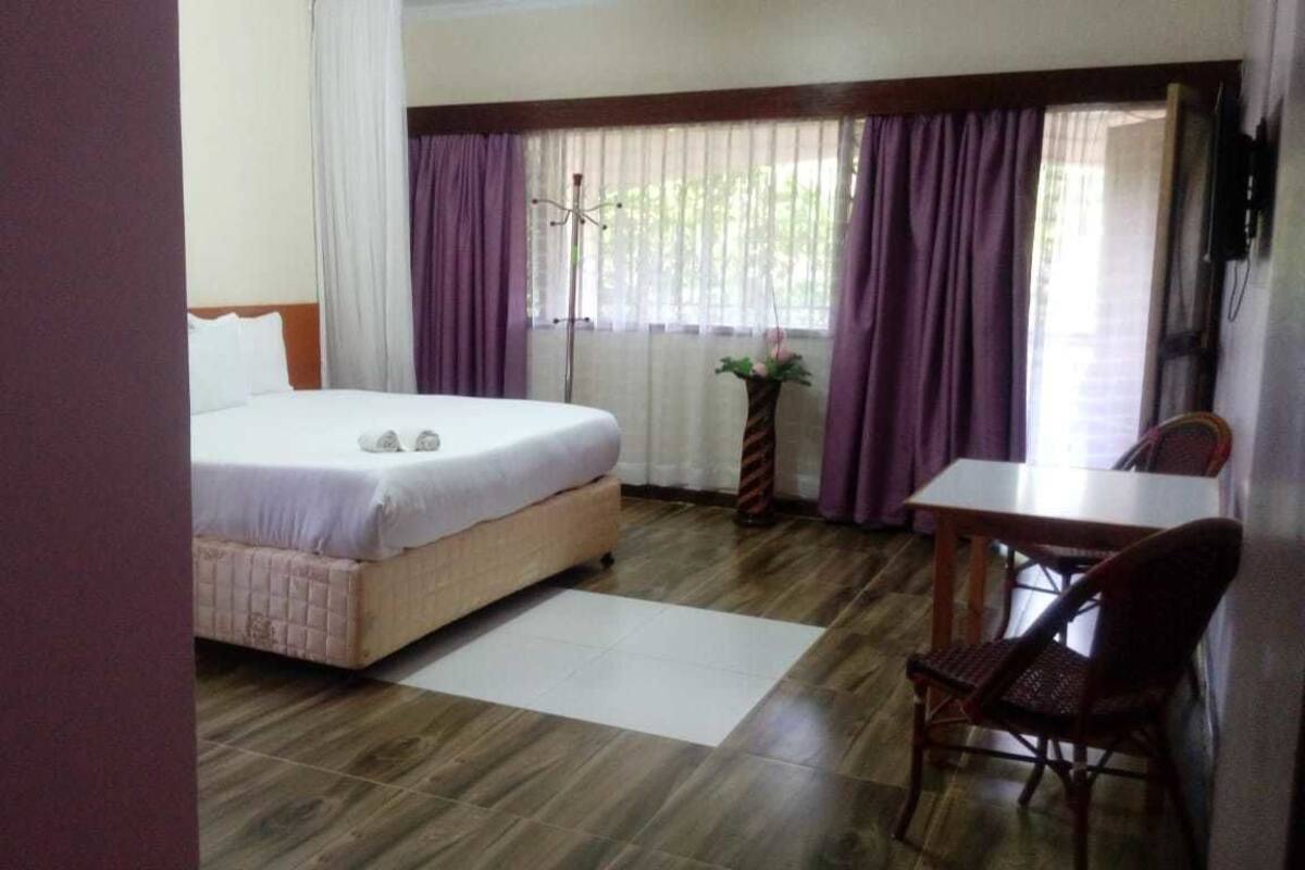 A hotel room with a bed, a desk, a chair, and a window with curtains.
