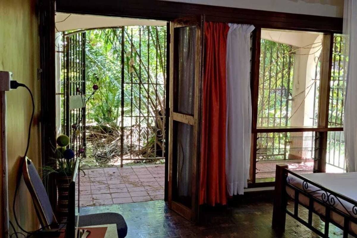A bedroom with a bed, a window with curtains, and a view of greenery outside.
