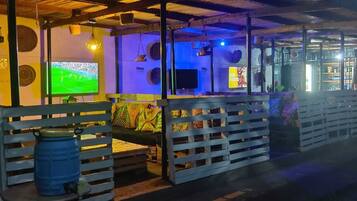 Un rincón de bar acogedor con televisión mostrando un evento deportivo, mobiliario de madera y una decoración rústica.