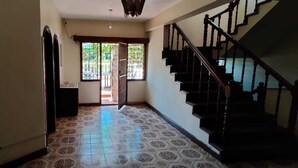 A hallway with patterned floor tiles, a staircase with wooden railings, and a door leading to an outdoor area with a view of greenery. - Tisa Suites & Lounge (Kisumu)