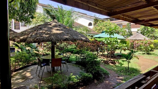 An outdoor patio area with a thatched umbrella, a round table, and chairs. - Tisa Suites & Lounge (Kisumu)