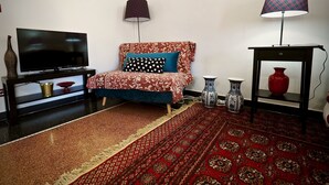 Ett vardagsrum med en soffa, en tv, dekorativa vaser och en mönstrad matta.