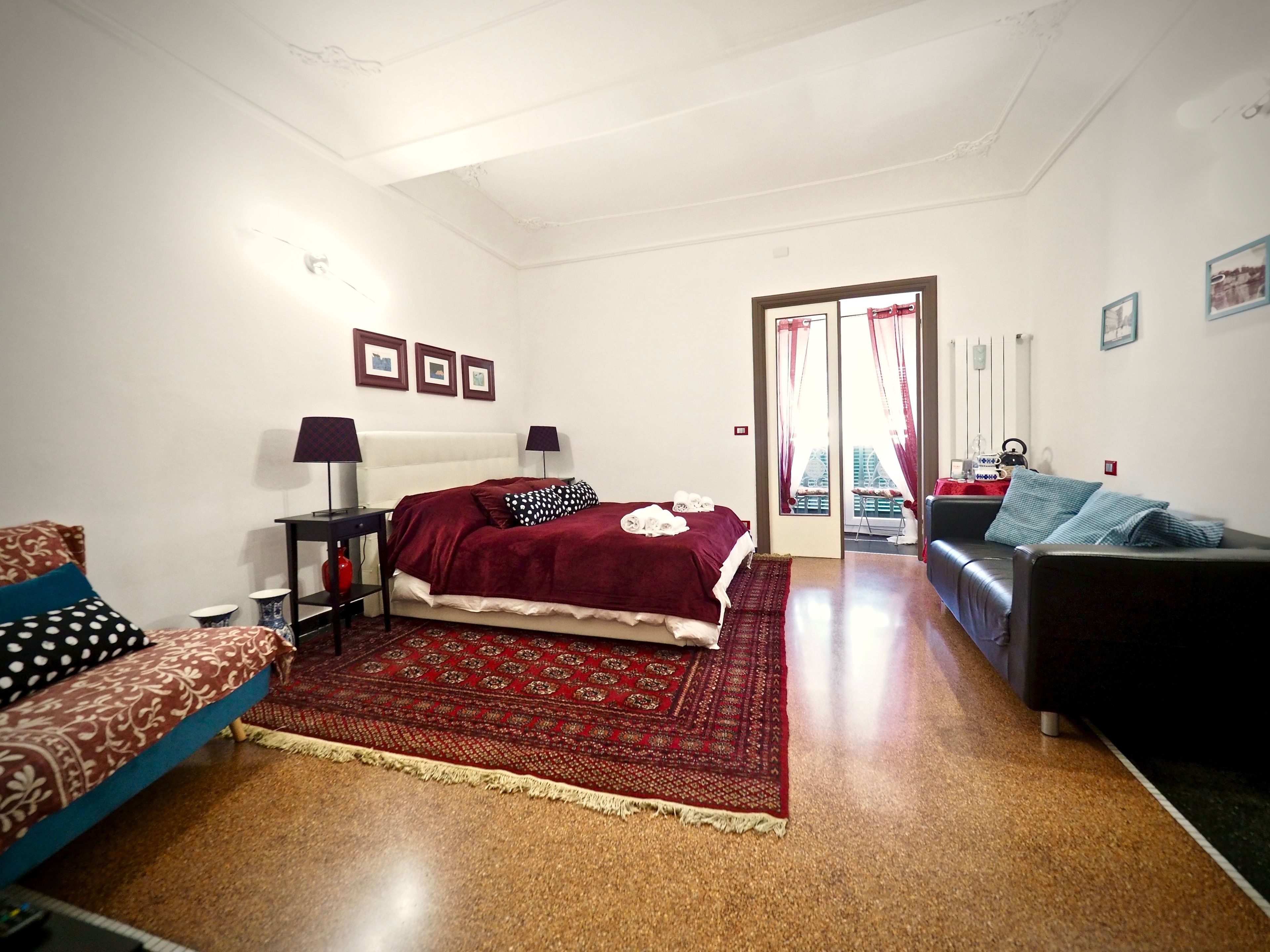 Une chambre à coucher avec un lit, deux tables de chevet, un tapis rouge à motifs, un canapé et un fauteuil.