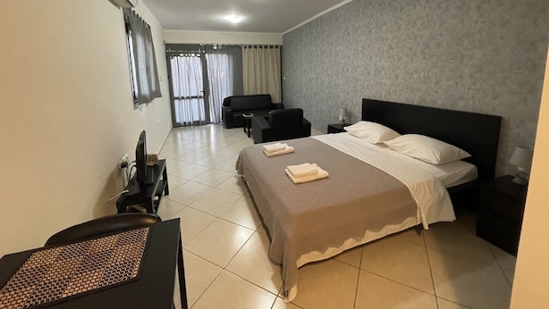 Habitación de hotel con cama, escritorio, silla, televisión y ventana con cortinas.