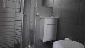 Un baño moderno con ducha de vidrio, lavamanos blanco y un inodoro.