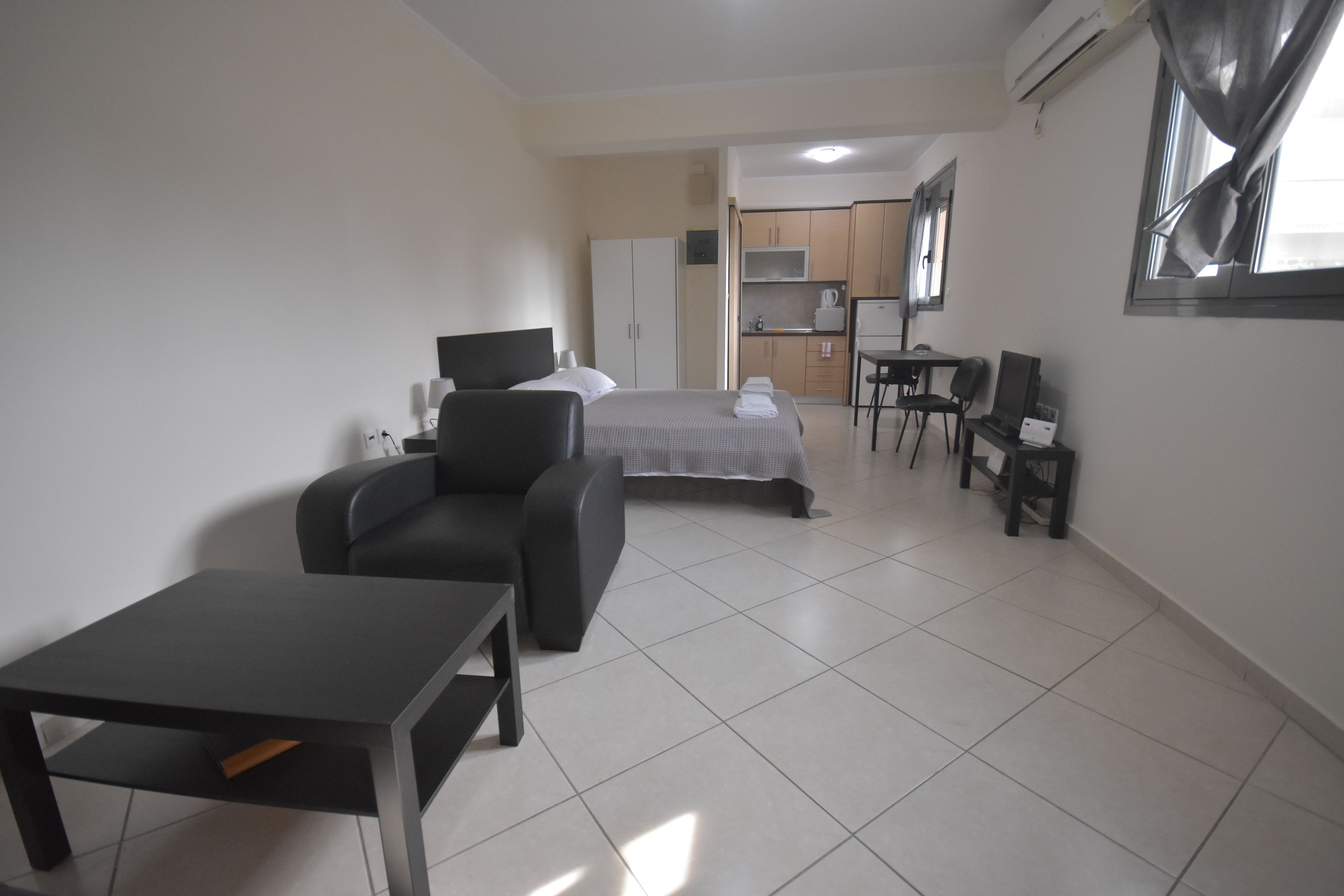 Habitación de hotel con cama, escritorio, silla, mesita, kitchenette y ventana con cortinas.