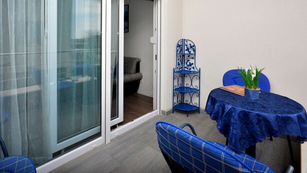 Un balcón con una mesa, sillas y una puerta corrediza de vidrio, además de una silla con estructura metálica decorativa.