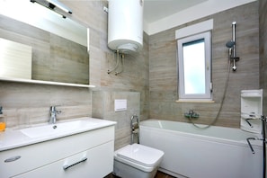 A modern bathroom with a white sink, toilet, and bathtub. - Apartment Jure (Podstrana)