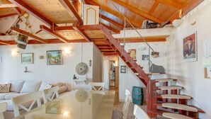 Zona d'estar àmplia amb escala de fusta, taula de menjador i sofà.