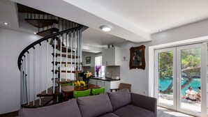 Un salon moderne avec un canapé gris, un coin repas avec une table et des chaises en bois, une cuisine à l’arrière-plan et un escalier.