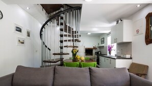 Un salon moderne avec un escalier en colimaçon, une table à manger verte ornée de fleurs jaunes et un canapé gris.
