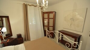 Un dormitorio con cama, mesita de noche, cómoda, espejo, lámpara de araña y una obra de arte en la pared.