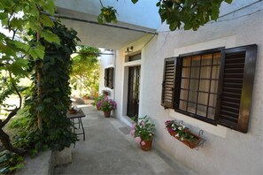 A covered outdoor area with a table and chairs, potted plants, and a building with shutters.