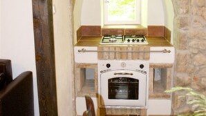 Una cocina con paredes de piedra, estufa y horno empotrados, un ventanal sobre el fregadero y una mesa de comedor con sillas.