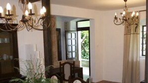 Un comedor con una mesa grande, sillas y una araña. Hay una planta sobre la mesa y una ventana con cortinas.