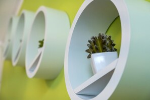A row of white cylindrical planters with small cacti against a green wall.