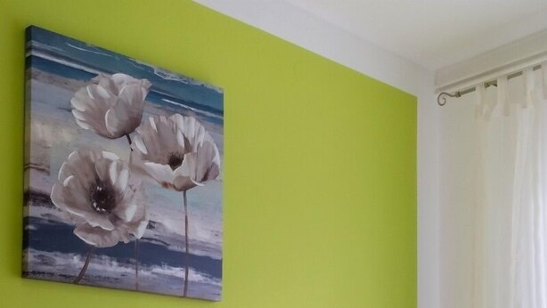 Une chambre à coucher avec une couvre-lit à motifs floraux, deux oreillers, un tableau représentant des fleurs accroché au mur et une serviette enroulée posée sur le lit.