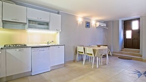 A compact kitchen with white cabinets, a dishwasher, and a dining area with a table and chairs. - Antonella - Apartment Nikola (Mali Losinj)