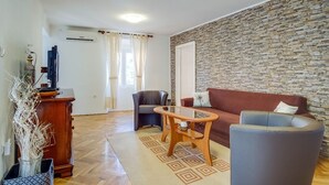 A living room with a stone wall, a sofa, a coffee table, and a chair. - Antonella - Apartment Antonella (Mali Losinj)