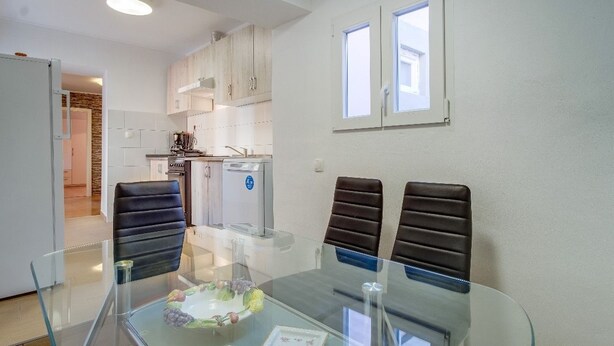 A modern kitchen with white cabinets, a built-in oven, and a coffee machine. There is a dining area with a glass table and two chairs. - Antonella - Apartment Antonella (Mali Losinj)
