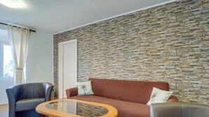 A room with a stone wall, a brown sofa, a glass-top table, and a dark leather armchair. - Antonella - Apartment Antonella (Mali Losinj)