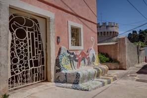 Ein Gebäude mit einem verzierten Metallgitter, einer Mosaikbank und einer schlossähnlichen Struktur im Hintergrund.
