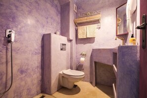 Ein kleines Badezimmer mit lila Wand, weißer Toilette, Dusche und Waschbecken inklusive Spiegel.