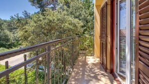 Un balcon doté d’une balustrade en métal, offrant une vue sur un paysage verdoyant et luxuriant ainsi que sur un grand arbre.