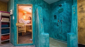 Une chambre avec un lit en bois, une porte en verre donnant sur une salle de bain équipée d’une douche et de deux robinets.