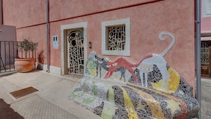 Un bâtiment aux murs roses, un banc en mosaïque et un portail en métal.