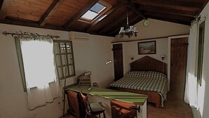 A bedroom with a wooden ceiling, a skylight, a bed with a checkered bedspread, a desk with a chair, and a small window with curtains.