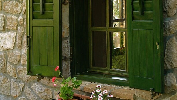A stone wall with a window featuring green shutters.