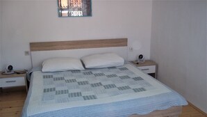 Una cama con cabecera de madera, almohadas blancas y colcha con estampado de cuadros.
