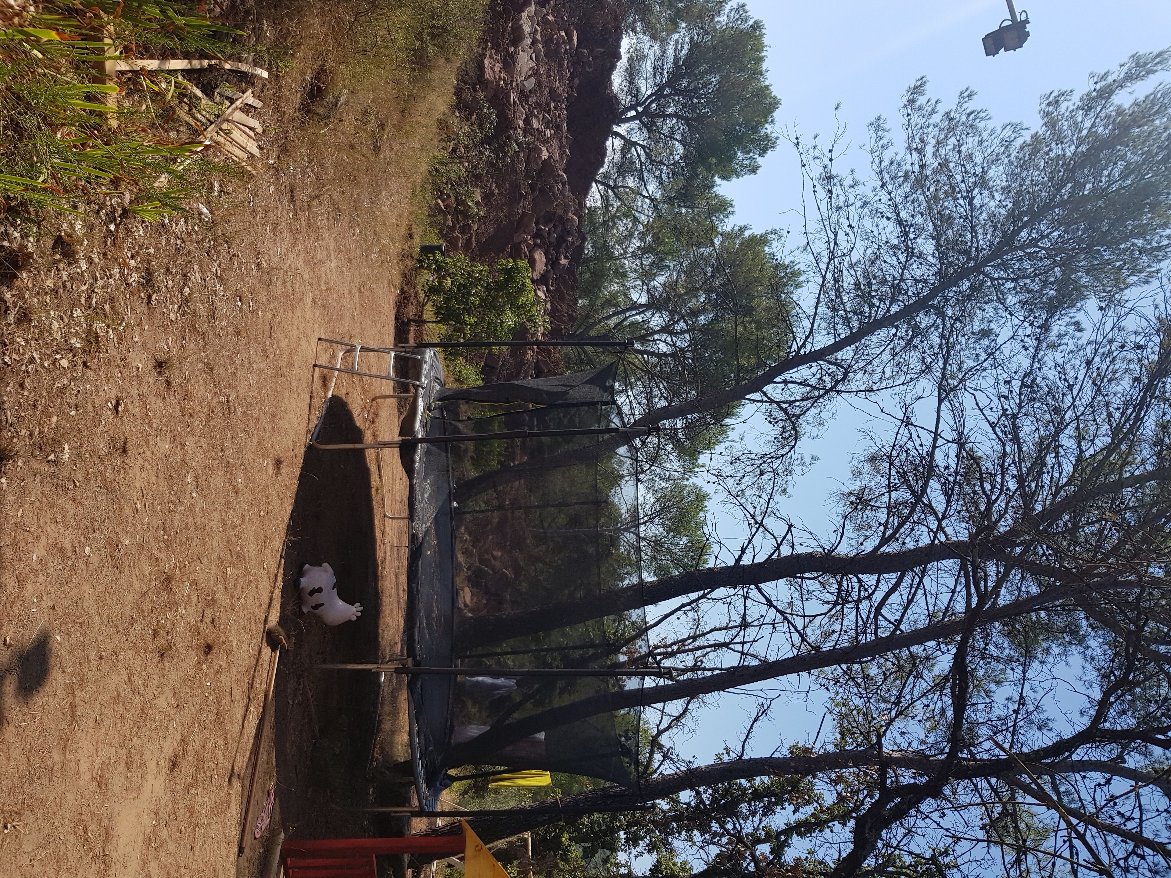 A dirt path leading to a covered area with metal railings, surrounded by trees and rocky terrain.