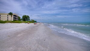A beach with a building on the left, a clear sky, and calm waves. - Kings Crown 210 (Sanibel)
