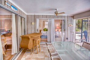 Ein sonnendurchflutetes Zimmer mit einem Glastisch, Holzstühlen und einem Deckenventilator.